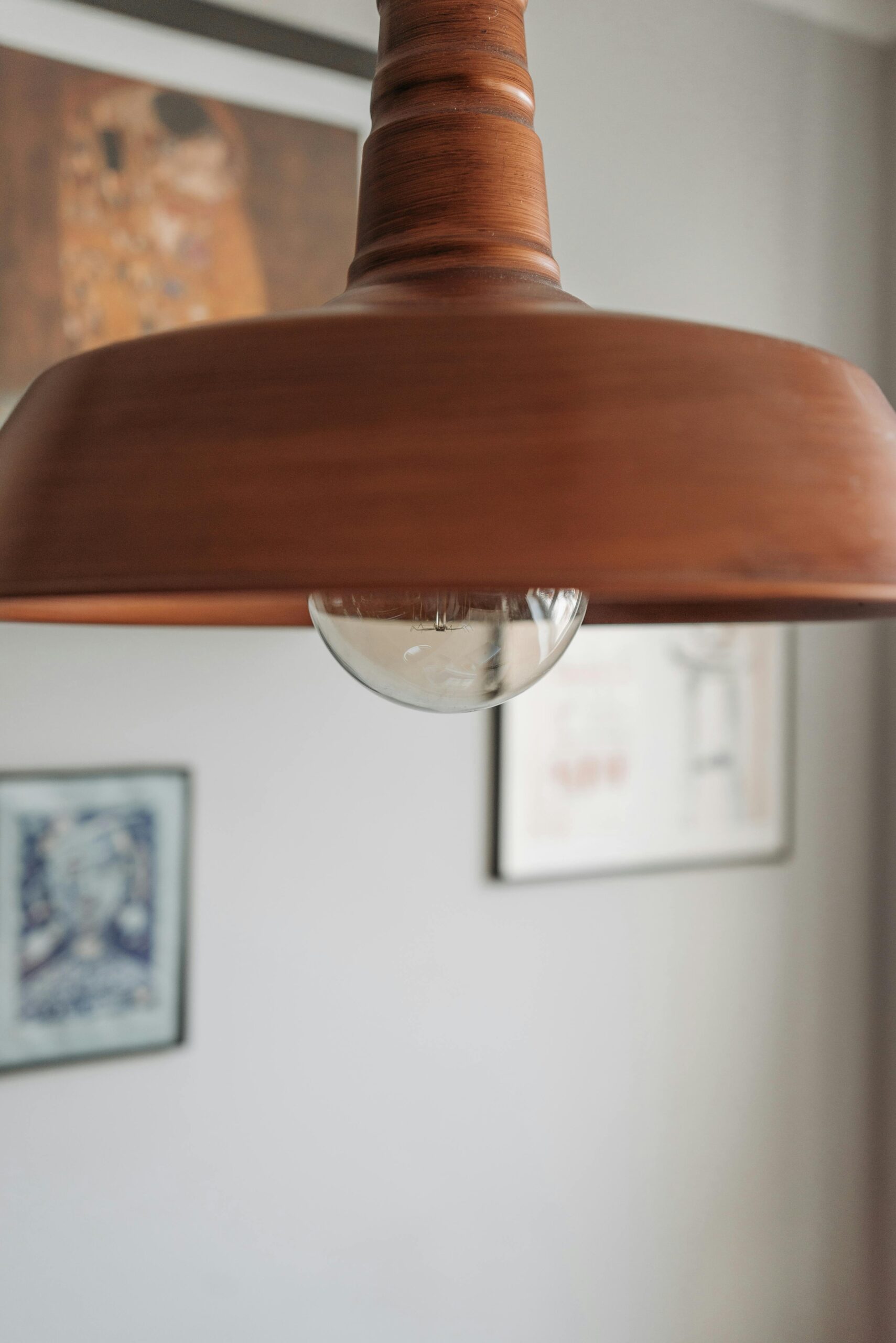 Close-up of a wooden hanging lamp with blurred artwork background.